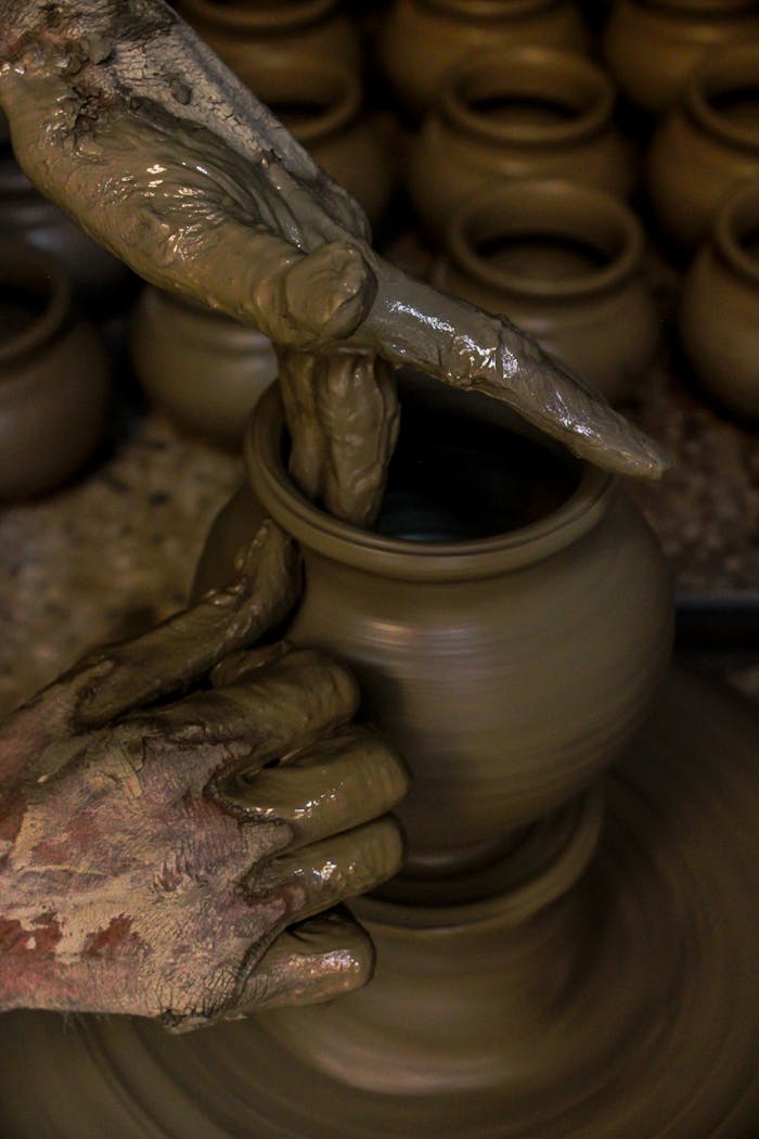 Intimate view of a potter's hands shaping a clay pot on a spinning wheel.